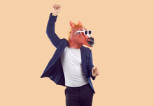 Portrait Of Strange Man Wearing T Shirt, Suit Jacket, Funny Horse Mask And Sunglasses Having Fun And Dancing Isolated On Beige Background. Fun, Party, Humor Concept