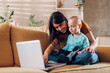 © Zamrznuti tonovi - Mother playing and hugging with her child son while using laptop at home