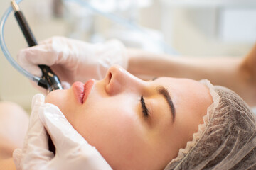 Wall Mural - Closeup headshot of young woman receiving hydrafacial therapy at beauty spa