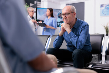 Wall Mural - Stressed tired senior patient sitting on chair in hospital lobby while waiting for specialist doctor to start medical examination during checkup visit consultation. Health care service and concept