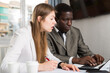 © JackF - African businessman and Caucasian businesswoman sitting at desk and working at office