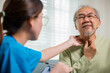 © sorapop - Asian young nurse checking senior man neck pain in clinic at retirement home, doctor woman examines lymph nodes on neck to determine if swollen, sore throat