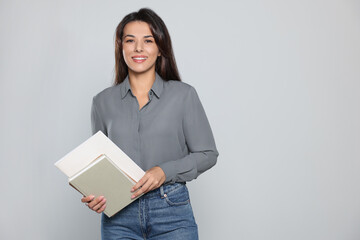 Wall Mural - Happy young teacher with books on light grey background. Space for text