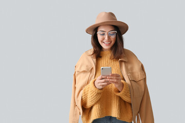 Poster - Young woman in hat using mobile phone on grey background