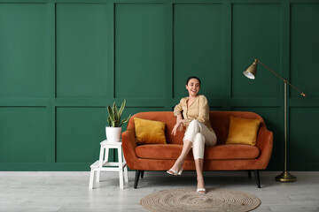 Poster - Young woman sitting on red sofa near green wall