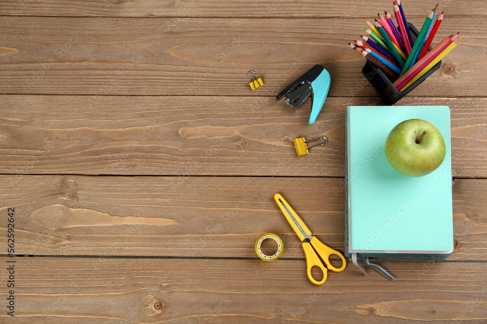 Pencils holder, notebooks with green apple, stapler and scissors on wooden background