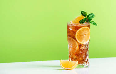 Wall Mural - Long Island ice tea cocktail with vodka, rum, tequila, gin, liquor, lemon juice, cola and ice, garnished with lemon slice and mint in highball glass. Green background