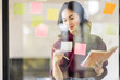 © David - Business female employee with many conflicting priorities arranging sticky notes commenting and brainstorming on work priorities colleague in a modern office.