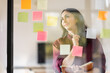 © David - Business female employee with many conflicting priorities arranging sticky notes commenting and brainstorming on work priorities colleague in a modern office.
