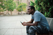 © alvaro - Man smiling while using mobile phone sitting on a bench outdoors.