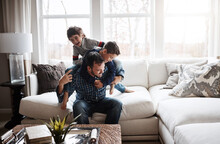 Playful, bonding and father with children on the sofa for playing, quality time and crazy fun. Love, happy and boy kids piling onto their dad with energy on the couch of their family home together