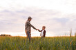 © Acronym - Farmer and his son in front of a sunset agricultural landscape. Man and a boy in a countryside field. Fatherhood, country life, farming and country lifestyle concept.