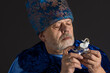 Nice low key portrait of bearded senior man in blue oriental clothes taking elephant porcelain figure and view it