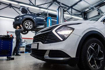 Selective focus on a car in foreground with auto mechanic repairing other car in blurry background.