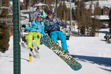 A Snowboarder And A Skier Ride The Chairlift Up The Mountain At A California Ski Resort.