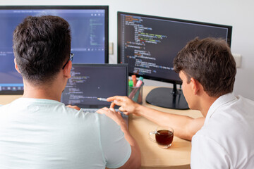 Two young programmers work on a programming project on a modern desktop computer with three monitors