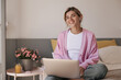 © Look! - Positive young caucasian girl with wireless headphones and laptop sitting on bed indoor. Smiling woman wears casual clothes at home. Concept gadgets, technologies.
