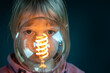 Young child looks concentrated through a filament light bulb. Symbol for a child curiously discovering the world.
