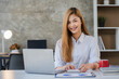 © ArLawKa - Asian female accountant or financial analyst looking at laptop screen taking notes and working at office with calculator documents on table Planning to analyze financial reports