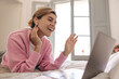 © Look! - Happy young caucasian woman use headphones speaking with friends over video link on laptop. Blonde female lying on bed and smiling at camera. Concept addiction to social media.