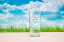Flowing Pure Water Into Tumbler On Grassland Landscape Background