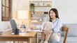 © Puwasit Inyavileart - Beautiful young asian woman watching live video or video call of teacher teaching on laptop in her home, Take notes of important conversations and messages during the teacher's teaching.
