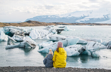 Mother with Daughter in Yellow Coat Walking on Glacial Lagoon in Iceland, Atlantic Ocean, Sunny Day