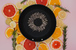 black frying pan with sunflower seeds, from which a sunflower flower is created on citrus plants cut into slices. Oranges, grapefruit, lemon, lime on a pink background. flat lay