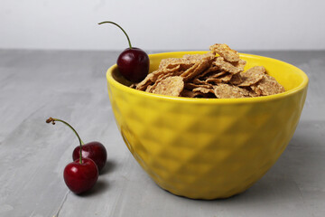 Canvas Print - healthy breakfast oatmeal corn flakes in a bowl of yellow with cherry berries on a gray background with space for text copyspace