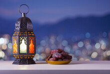 Holy Month Of Ramadan Concept. Righteous Muslim Lifestyle. Ramadan Lantern (Fanous), Dates.. Mountains And City Lights In Bokeh Blurred Background. Copy Space
