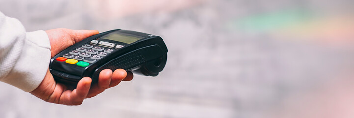 Man holds a payment terminal for cashless payments in his hand, against the background of a concrete wall.