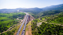 Aerial View Shot Flying Over Green Hills Fields, Presents Highway Road And Modern Bridge With Driving Cars. Curvy Road Through Green Mountains