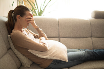 Wall Mural - Exhausted tired woman at home sitting on sofa with hand over face  