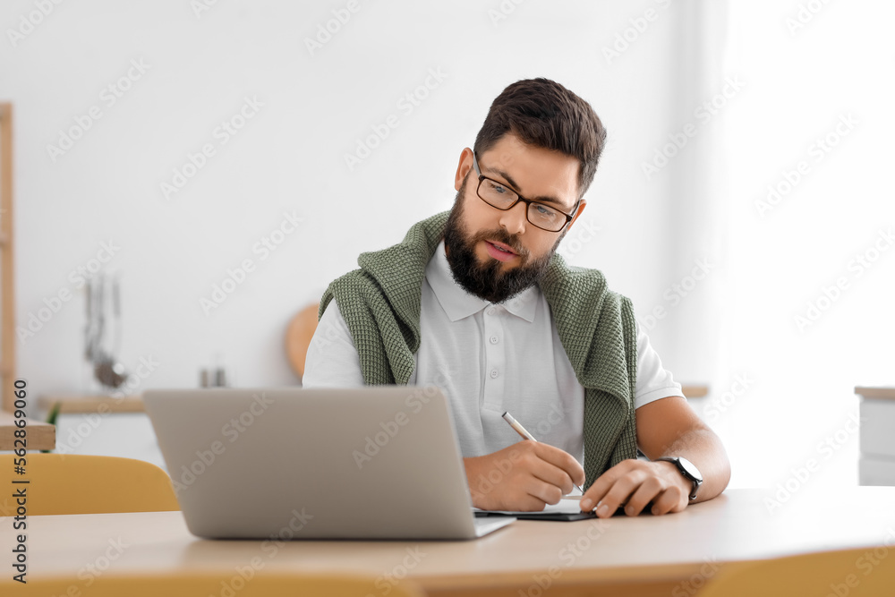 Male psychologist with laptop video chatting at table in kitchen