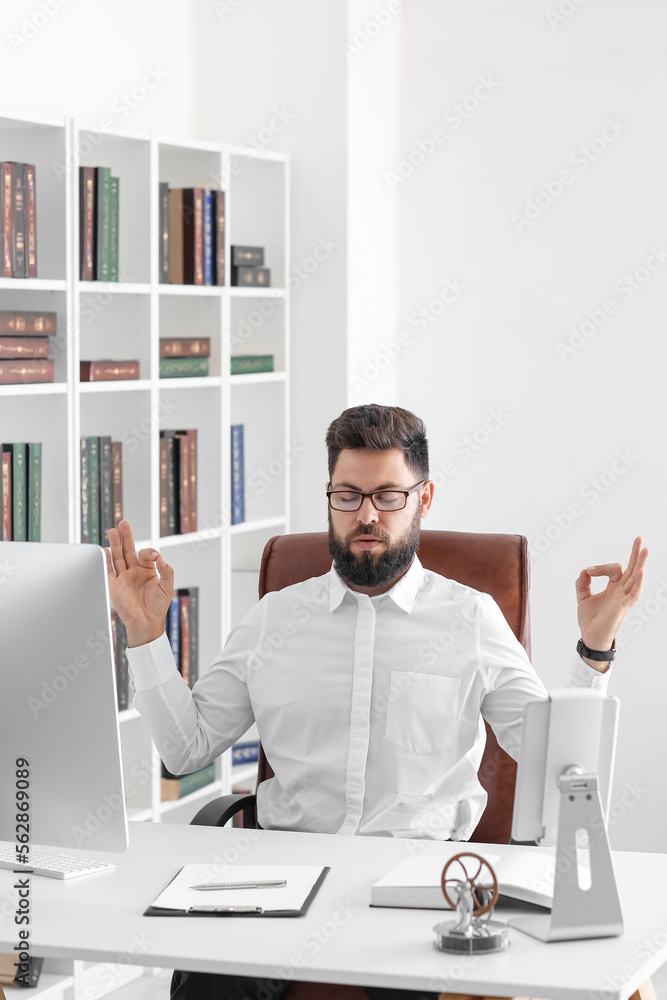 Handsome young man meditating at table in office