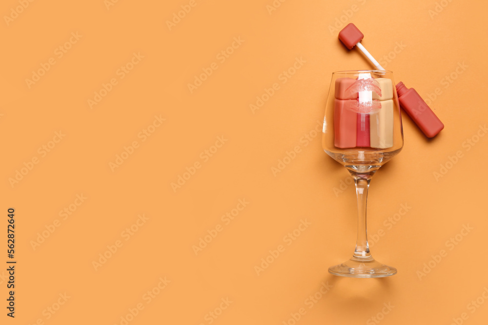 Glass with lipsticks and kiss mark on orange background