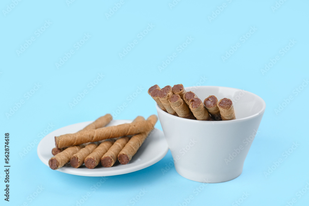 Plate and bowl with tasty wafer rolls on blue background