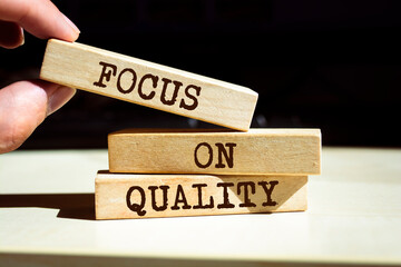 Wall Mural - Closeup on businessman holding a wooden blocks with text 'FOCUS ON QUALITY', business concept