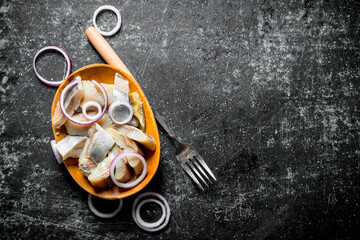 Canvas Print - Pieces of salted herring on a plate with a fork and sliced onions.