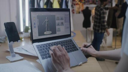 Female fashion designer develops future design of clothes in 3D modeling program on laptop using digital tablet and stylus. She works in atelier workshop. Fashion and technologies in business concept.