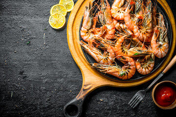 Wall Mural - Grilled shrimps on a cutting Board with tomato sauce and sliced lemon.