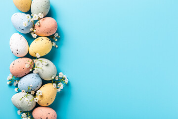Wall Mural - Easter quail eggs and springtime flowers over blue background. Spring holidays concept with copy space. Top view