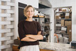 © nataliaderiabina - Portrait of smiling young woman entrepreneur standing at the counter of her bakery and coffee shop. Local small business owner indoors.