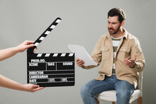 Emotional Actor Performing While Second Assistant Camera Holding Clapperboard On Grey Background, Closeup