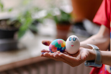  Funny painted eggs in the hands of a child. Easter celebration is a Christian tradition. Entertainment with children. Drawing on the egg in the form of a funny face muzzle
