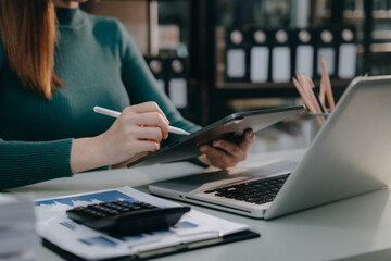 Business woman working on tablet to calculate financial data report, accountancy document and laptop computer at office, business concept.