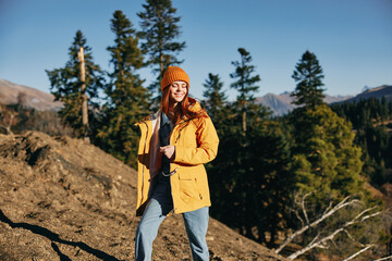 Sticker - Woman hiking in the mountains in the autumn, a smile and happiness in a yellow cape with red hair full-length standing in front of trees and mountains in the sunset light