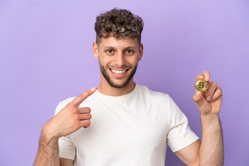 Wall Mural - Young caucasian man holding a Bitcoin isolated on purple background giving a thumbs up gesture