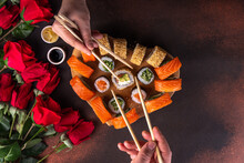 Heart Shaped Valentine Day Sushi Set. Classic Sushi Rolls, Philadelphia, Maki Set For Two, With Two Pairs Of Chopsticks For Valentine's Dating Dinner, With Rose Flowers Bouquet On Dark Background