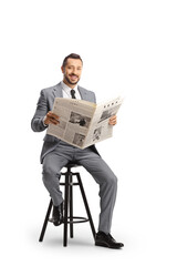 Young professional man in a suit sitting on a chair with a newspaper and smiling at camera